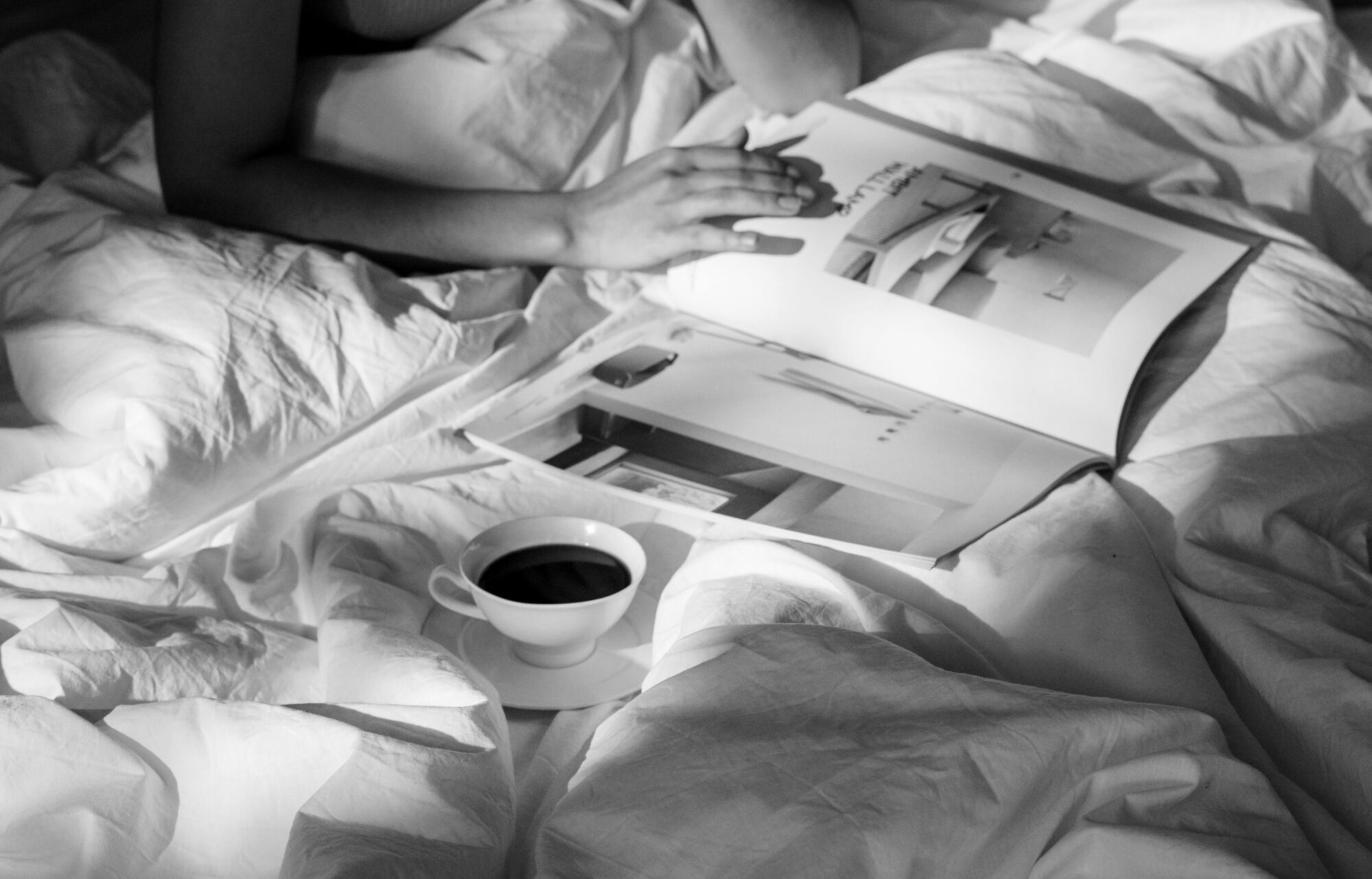 Woman reading a magazine on her bed with a cup of tea